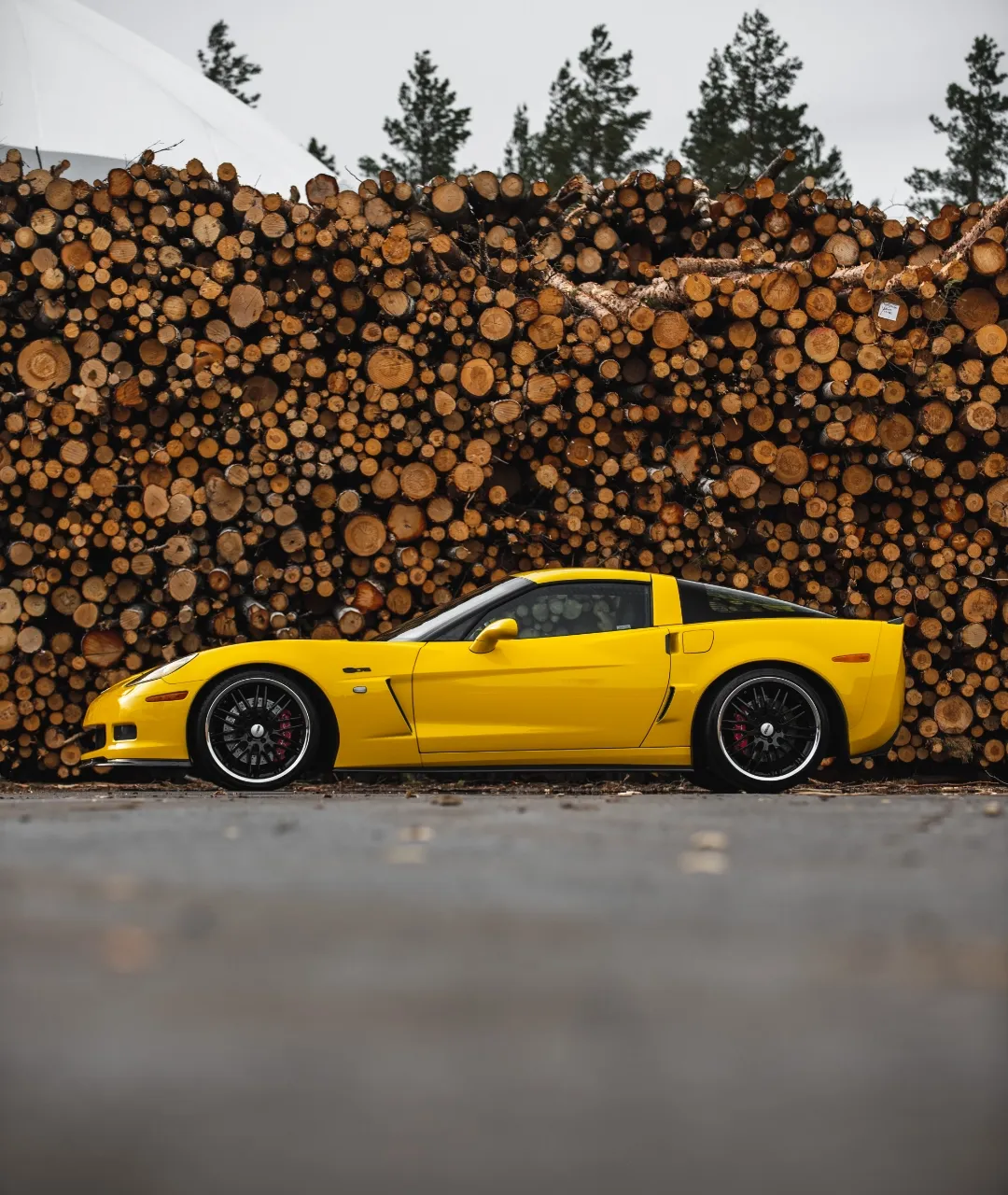 Keltainen Corvette kuvattuna puupinon edessä