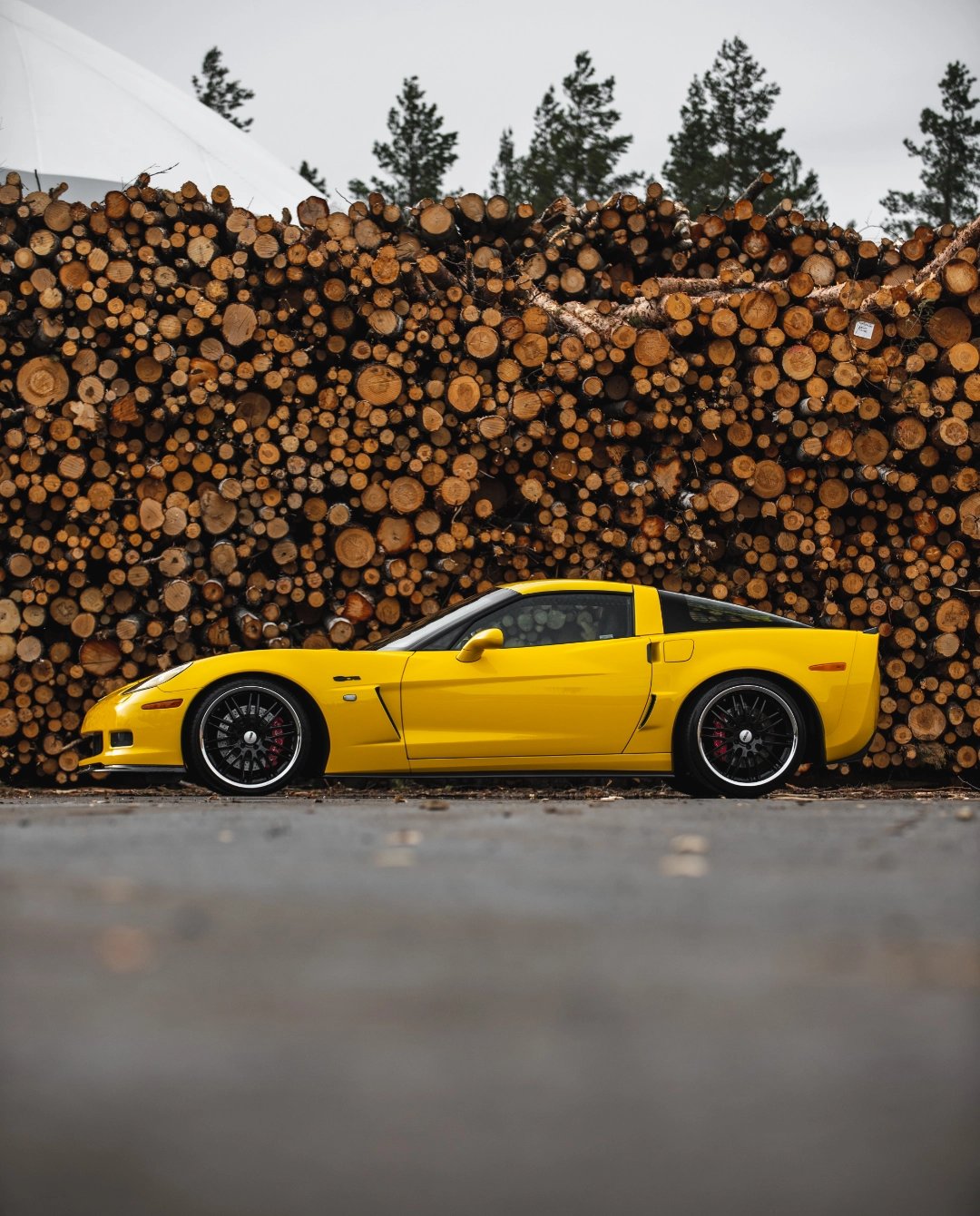 Keltainen Corvette kuvattuna puupinon edessä